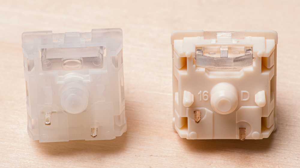 A close-up of two lightly colored mechanical switches. The one on the left has two electrical pins and a center post, while the one on the right also has two stabilizing posts on both sides.