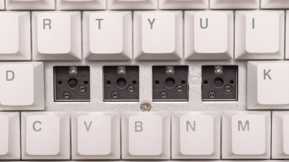 A close-up of the center row of a keyboard with the key switches removed. You can see the holes in the PCB made for the stabilizing post on both sides of the center post.