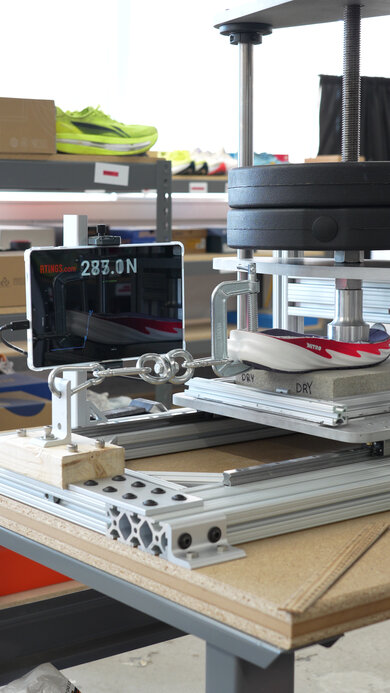 Shoe traction test rig pressing a weighted foot onto a running shoe outsole on a dry concrete slab, with a tablet displaying 283.0 N of friction force.